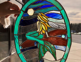 A blond mermaid from behind, sitting on a rock in the sea, all stained glass