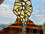 a blond girl with one french braid, wearing a red and orange checkered shirt, from behind, made of stained glass