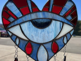 A heart shape with a crying eye inside, tears chained and hanging below, all stained glass