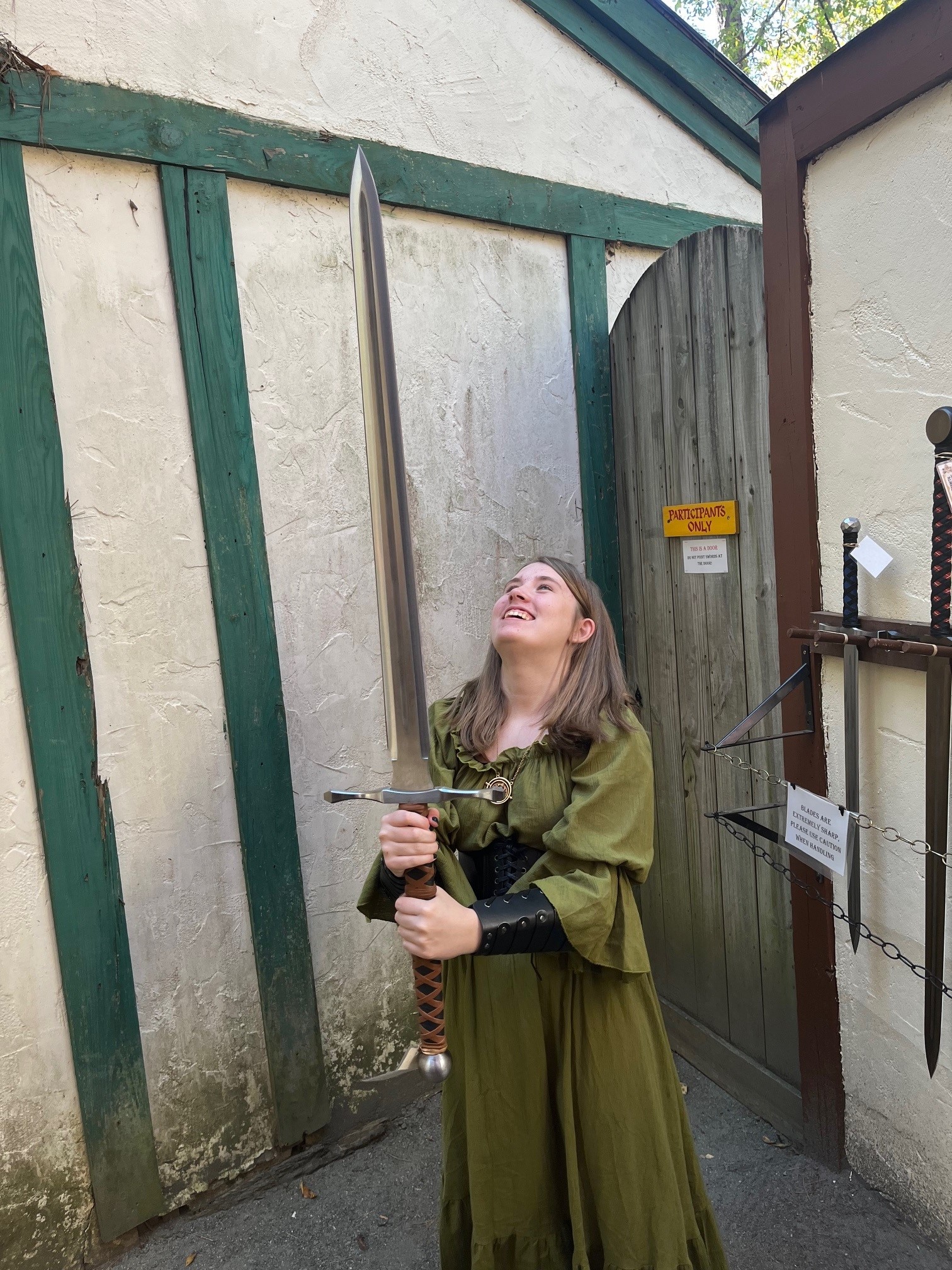 student holding fake sword in renaissance garb, smiling up at blade